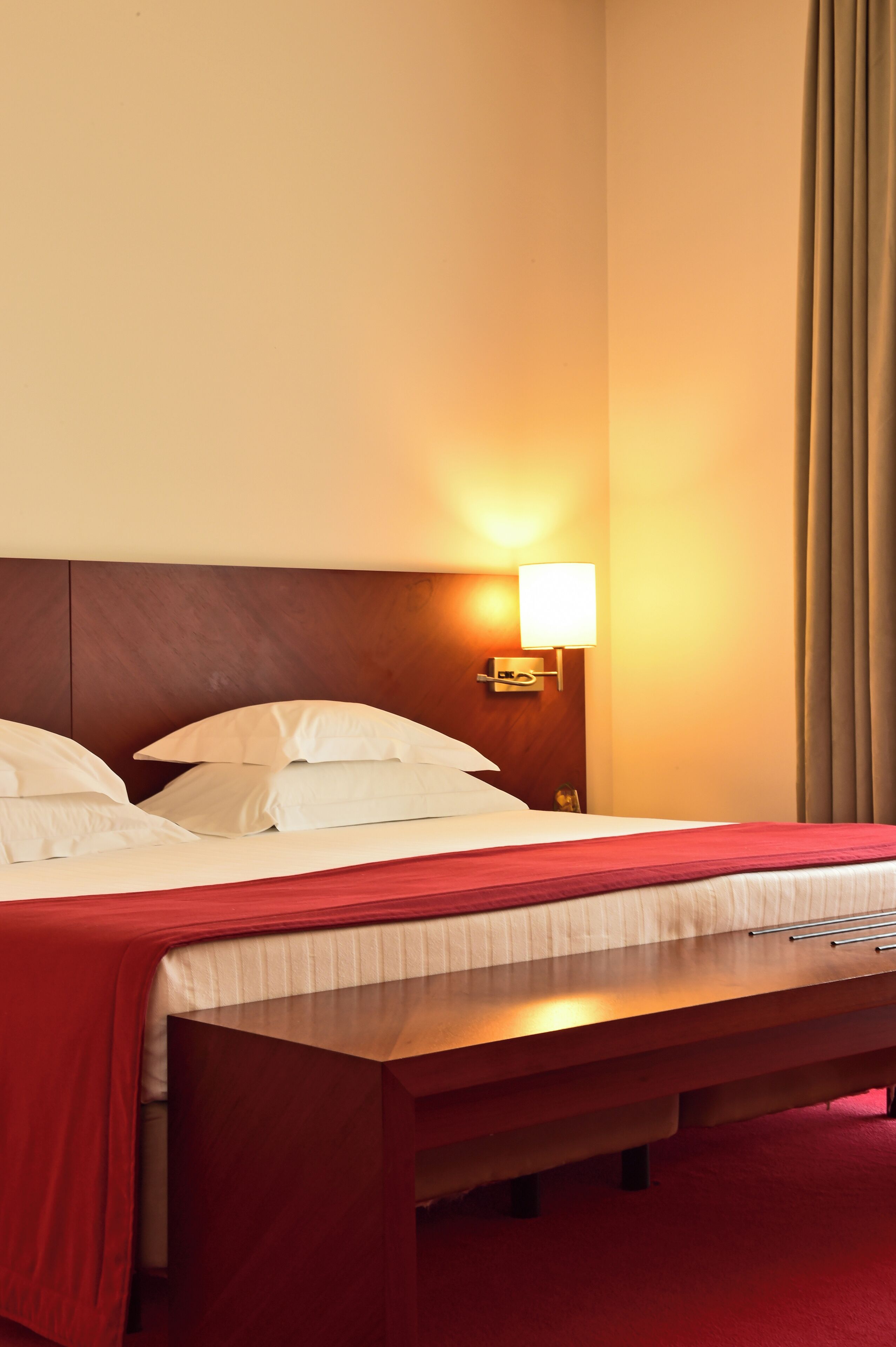 A hotel room with a bed, a bedside table, a lamp, and a window with curtains.