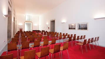 Une salle de conférence avec des rangées de chaises, un tapis rouge et deux tableaux encadrés accrochés au mur.