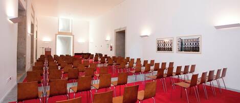 A conference room with rows of chairs, a red carpet, and two framed pictures on the wall.
