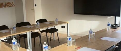 Un salón de conferencias con una larga mesa, sillas, botellas de agua y un televisor de pantalla plana en la pared.