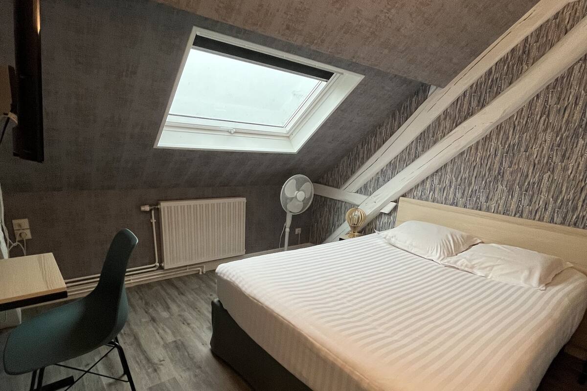 Une chambre avec une lucarne, un lit, un bureau et une chaise.