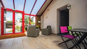 A sunlit room with a glass door leading outside, wicker furniture, a table with chairs, and a lamp. - Hôtel De Troyes   (Troyes)