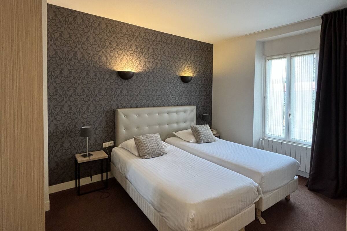 Un lit double avec une tête de lit capitonnée, deux tables de chevet, une lampe et une fenêtre avec des rideaux.