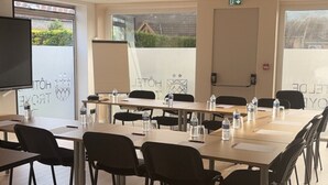 A conference room with multiple tables and chairs, a projector screen, and windows with a view of greenery and buildings. - Hôtel De Troyes   (Troyes)