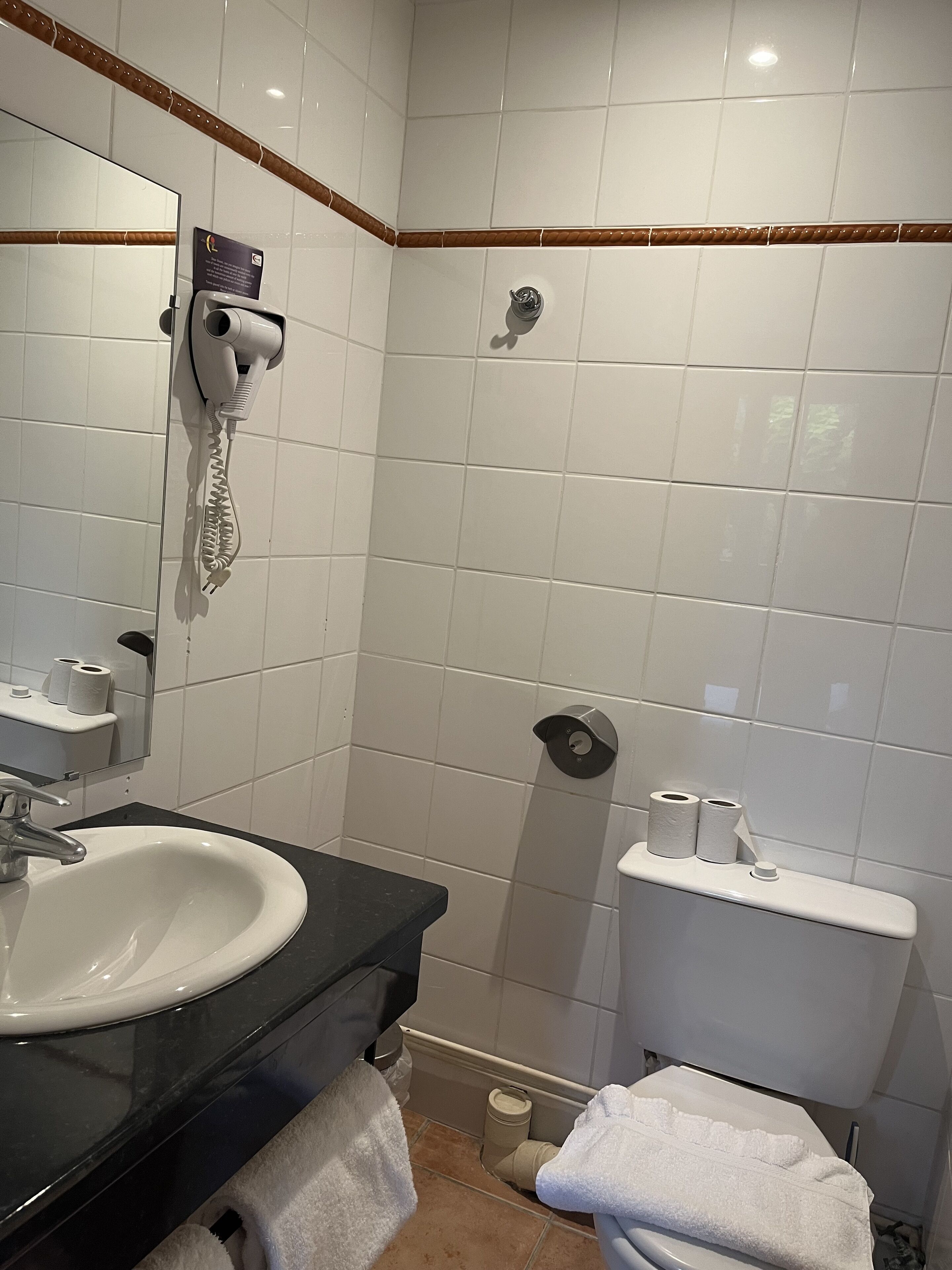 Un baño con lavamanos blanco, un espejo, toallero, inodoro y zona de ducha.