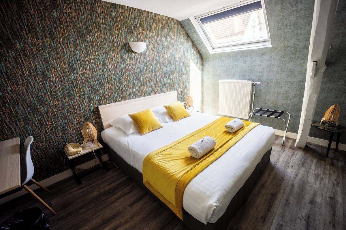 Une chambre d’hôtel moderne dotée d’un grand lit, d’une lucarne, d’un radiateur et d’un bureau avec une chaise.