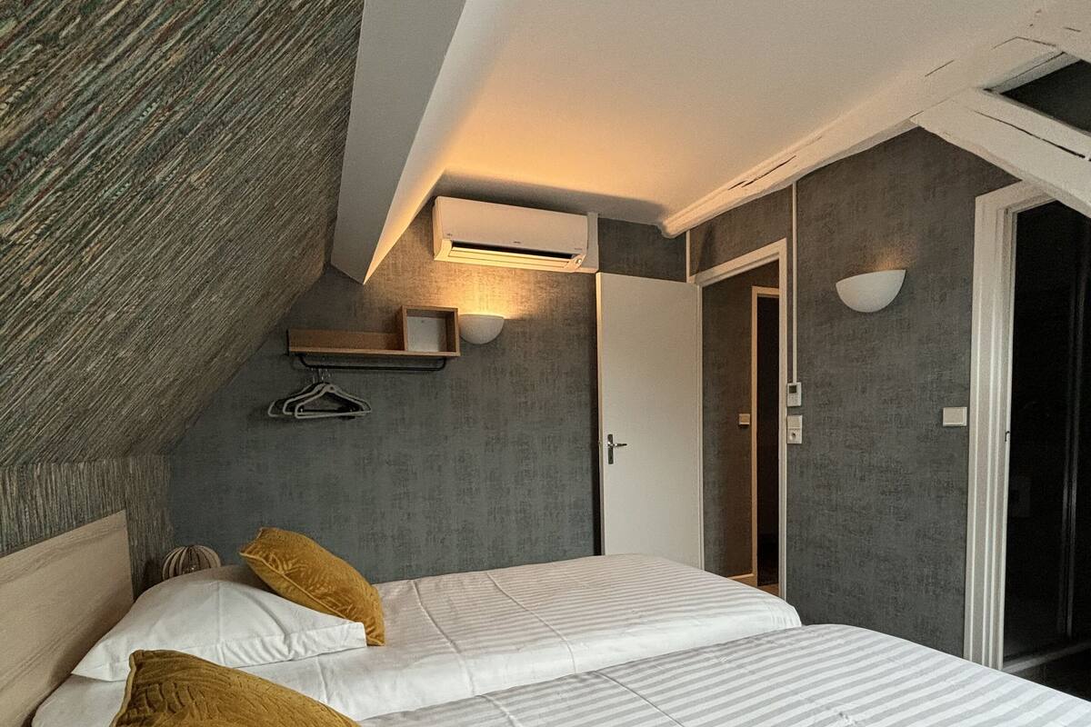Une chambre avec deux lits, un plafond en pente, une étagère intégrée et une porte donnant sur une autre pièce.