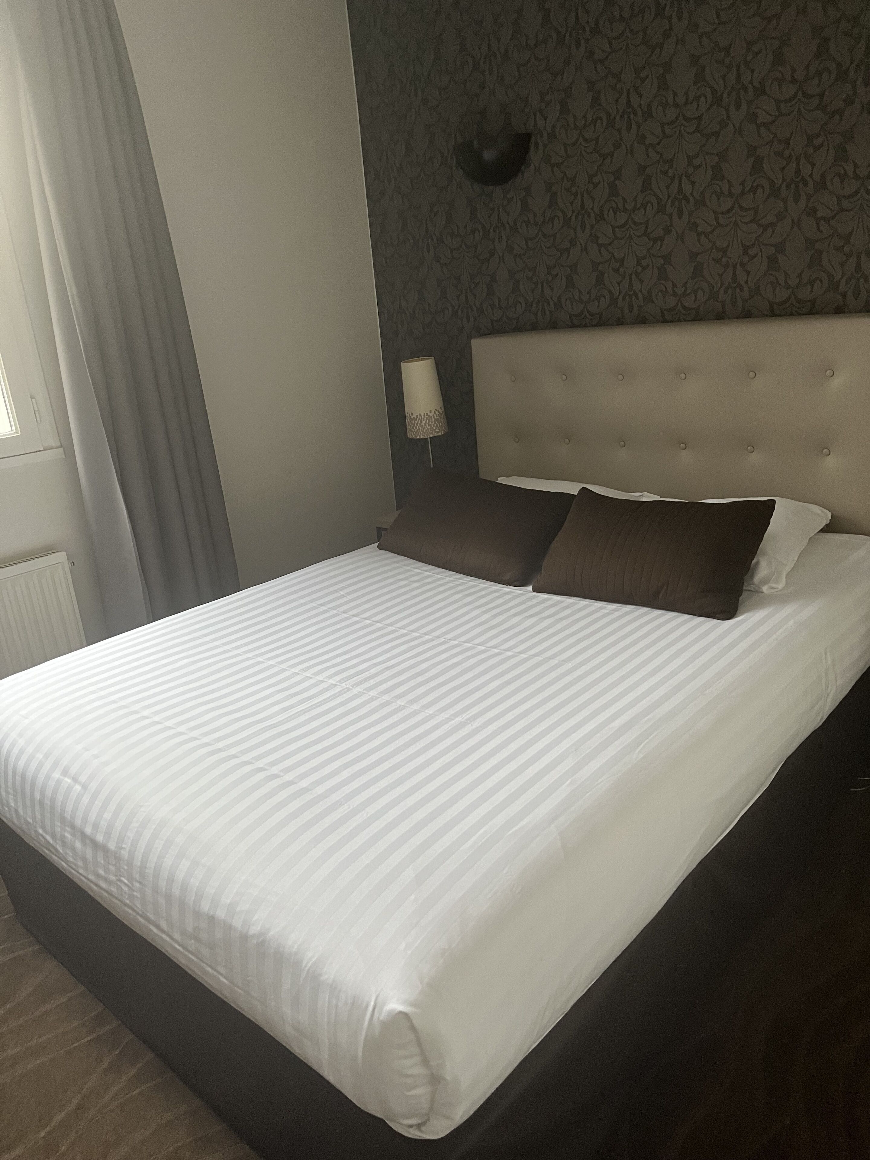 A neatly made bed with a striped white duvet, a dark headboard, and two dark pillows.