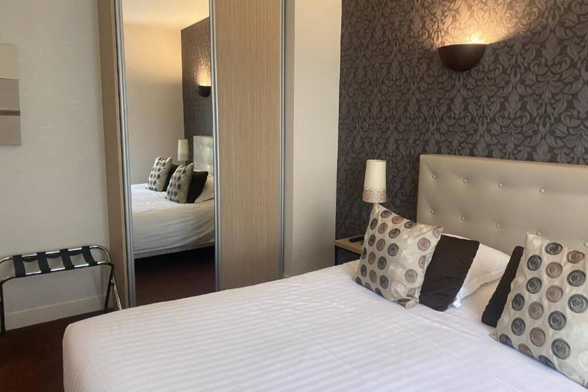 Une chambre d’hôtel avec un grand lit, un miroir, une table de chevet et une lampe fixée au mur.