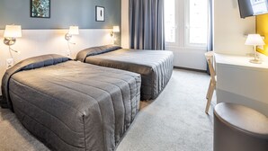 A hotel room with two beds, a desk, a chair, a TV, and a window with curtains. - Hôtel Mirasol (Lourdes)