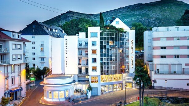 A modern hotel with a central atrium, multiple floors, and a view of a mountain. - Hôtel Mirasol (Lourdes)