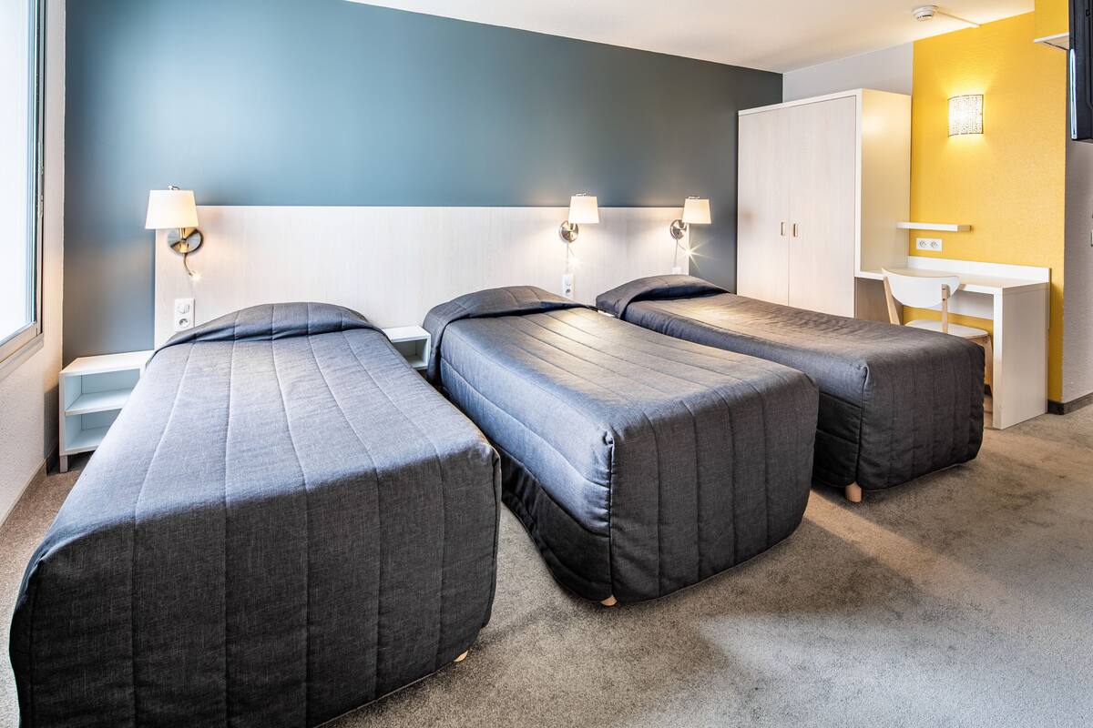 Et hotelværelse med tre enkeltsenge, et skrivebord og et klædeskab.