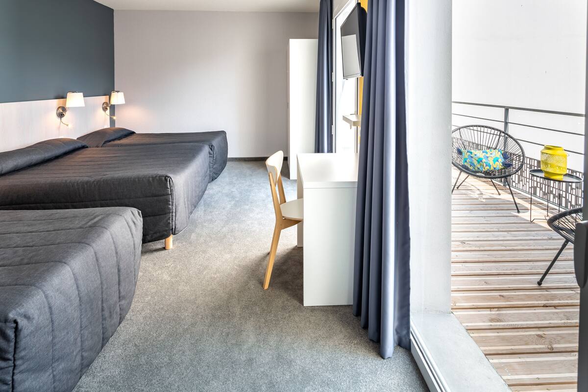 Et hotelværelse med to senge, et skrivebord, en stol og en balkon med en stol og en gul lanterne.