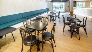 A modern dining area with wooden flooring, black metal chairs, and tables. There is a blue bench along the wall and a glass door leading outside. - Hôtel Mirasol (Lourdes)