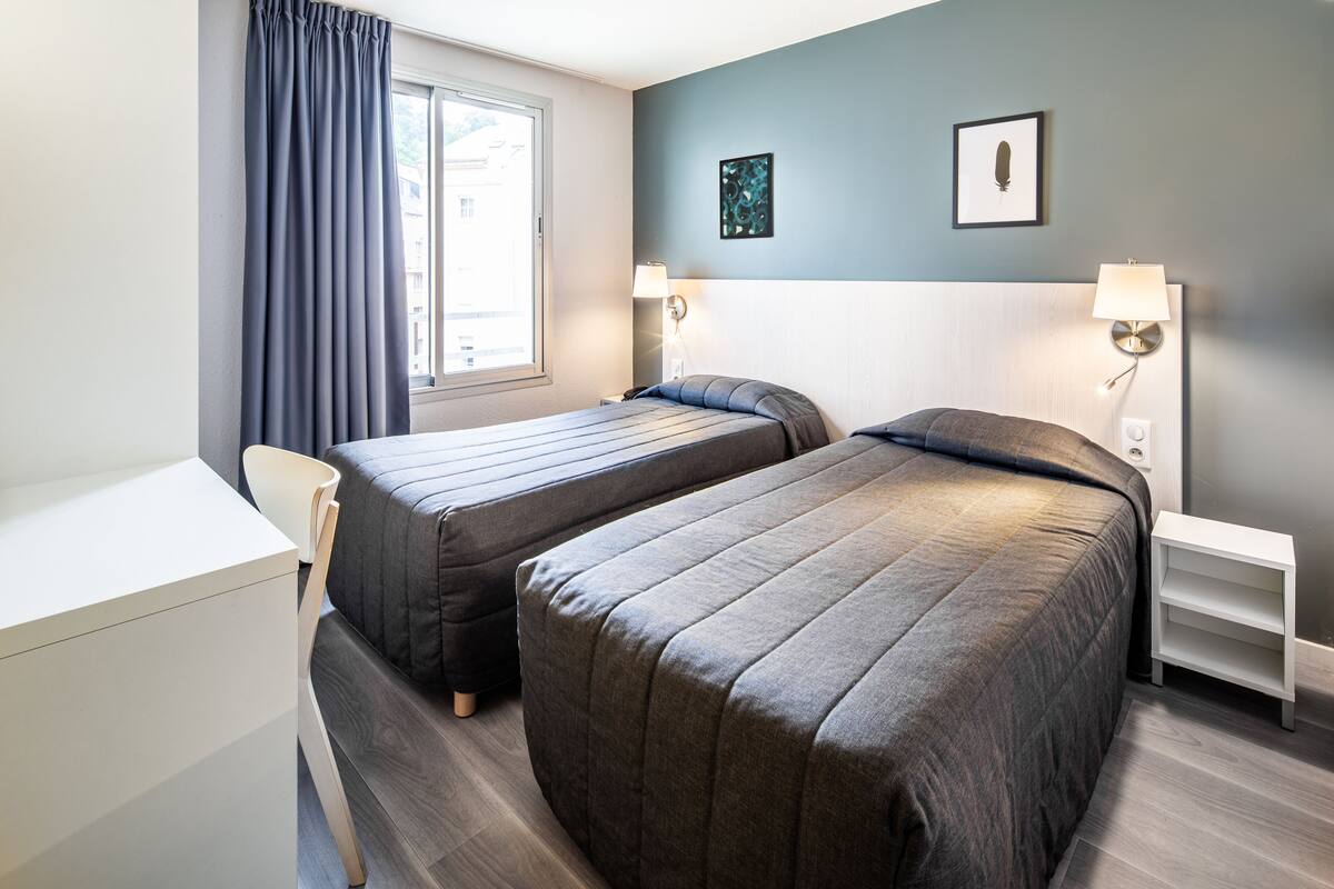 Et hotelværelse med to senge, et skrivebord og en stol.