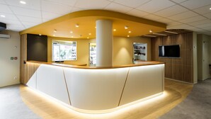 A reception area with a curved counter, a large pillar, and a flat-screen TV mounted on a wooden panel wall. - Hôtel Mirasol (Lourdes)