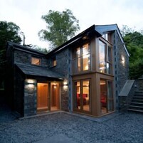 A modern two-story stone house with large windows and a stone facade.