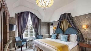 Una camera d'albergo con un letto grande, due poltrone, un tavolino e una finestra con tende.