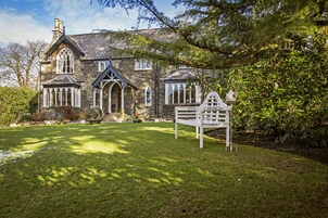 A stone house with a well-maintained lawn, a white bench, and a birdhouse.