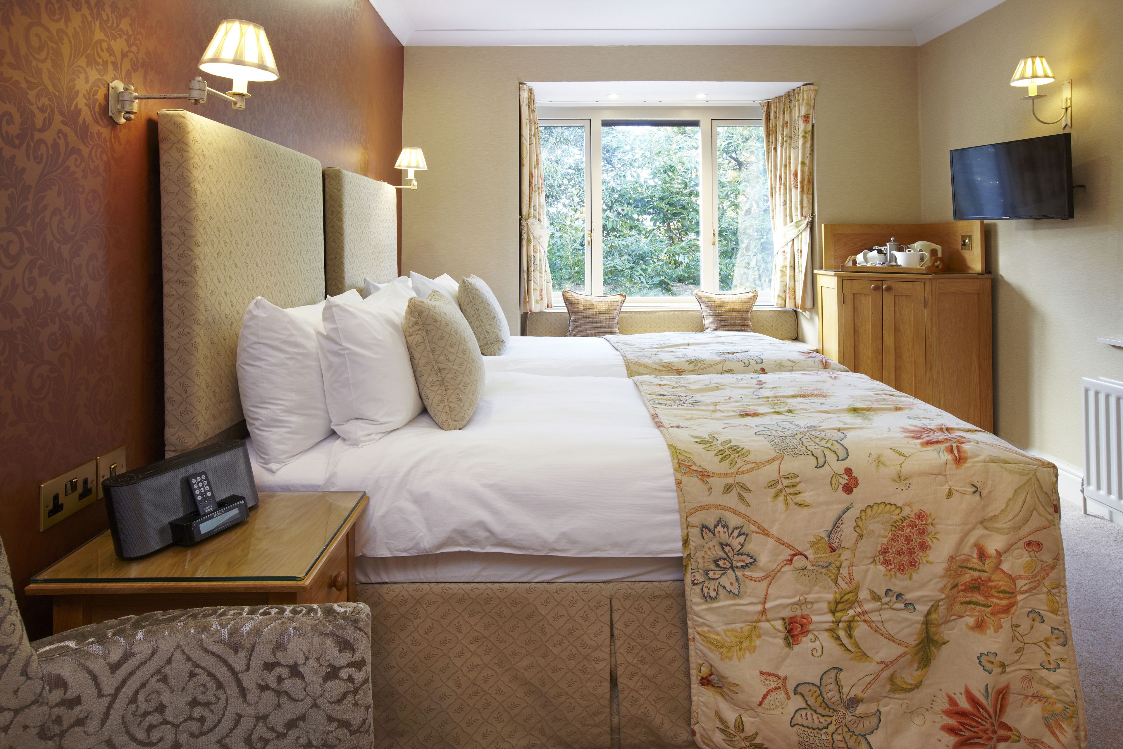 Quarto de hotel com uma cama grande, luminárias de cabeceira, televisão e uma janela com cortinas.