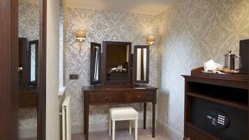 A bathroom with a vanity, two wall-mounted mirrors, a radiator, a bench, and a shelf with a coffee pot.