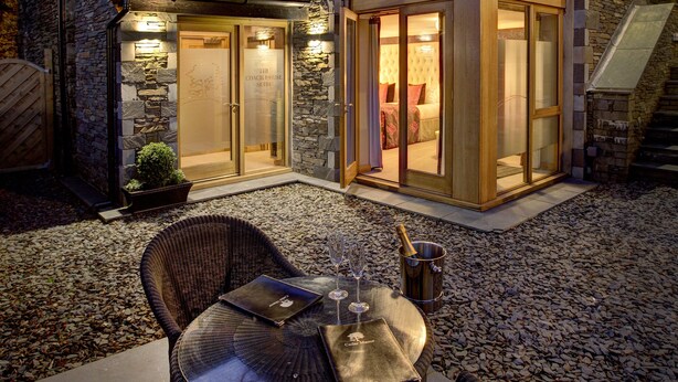 Una moderna casa a due piani con facciata in pietra, ampie vetrate e un patio con mobili in vimini.