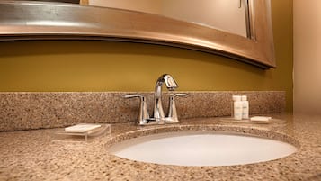 A bathroom sink with a single faucet, a mirror above it, and two toiletry bottles on the counter.