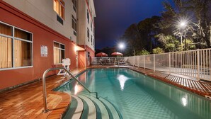 An indoor swimming pool with a wooden deck, a white fence, and a red building in the background. - Best Western Plus Jacksonville West (Jacksonville)