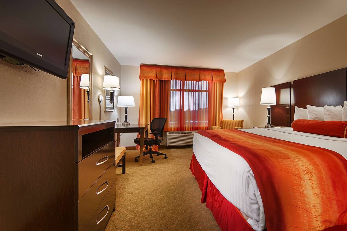 A hotel room with a bed, desk, chair, and a television.