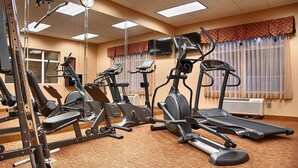 A fitness center with various exercise machines, a television, and a large window with curtains. - Best Western Plus Jacksonville West (Jacksonville)