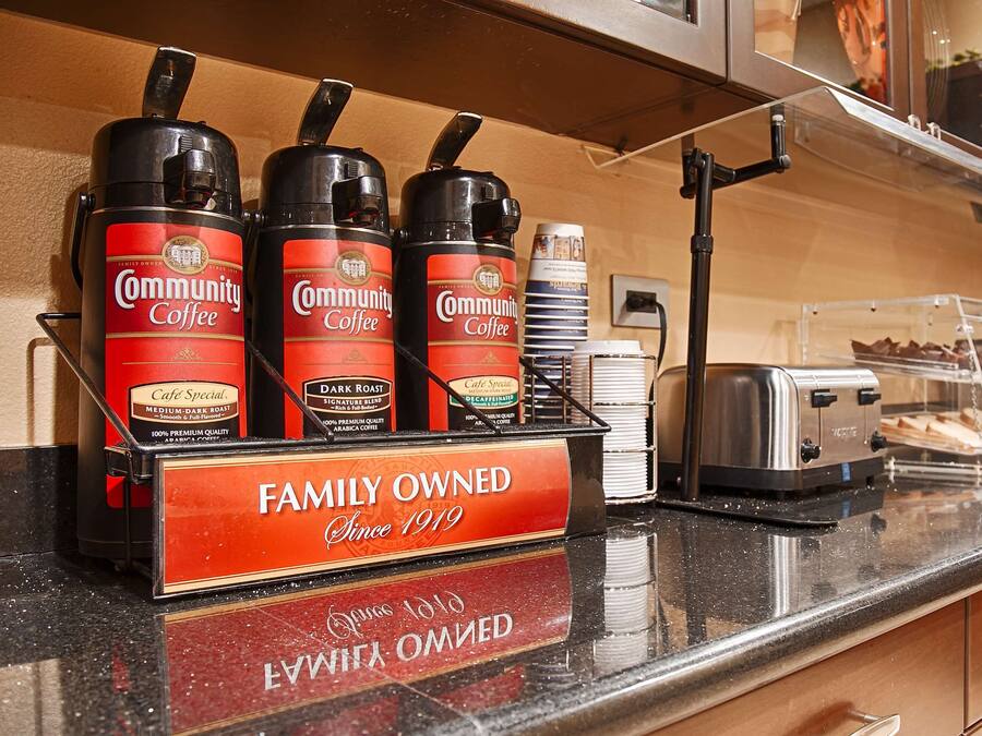 A coffee station with multiple coffee dispensers, a toaster, and a display case with pastries.