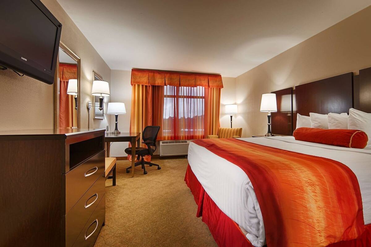 A hotel room with a bed, desk, chair, and a television.