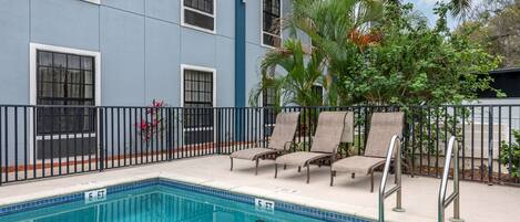 A swimming pool with lounge chairs and a metal fence.