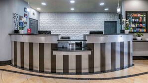 A reception area with a modern design, featuring a curved reception desk, a patterned wall, and a ceiling with recessed lighting. - Best Western Plus Bradenton Gateway Hotel (Bradenton)