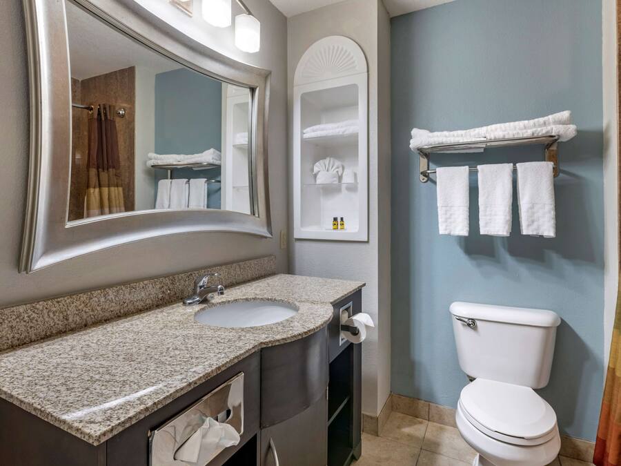 A bathroom with a granite countertop sink, a mirror, a towel rack, and a toilet.