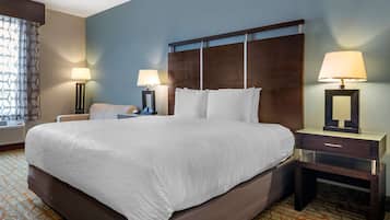 Habitación de hotel con una cama grande, dos mesitas de noche con lámparas, una silla y una alfombra estampada.