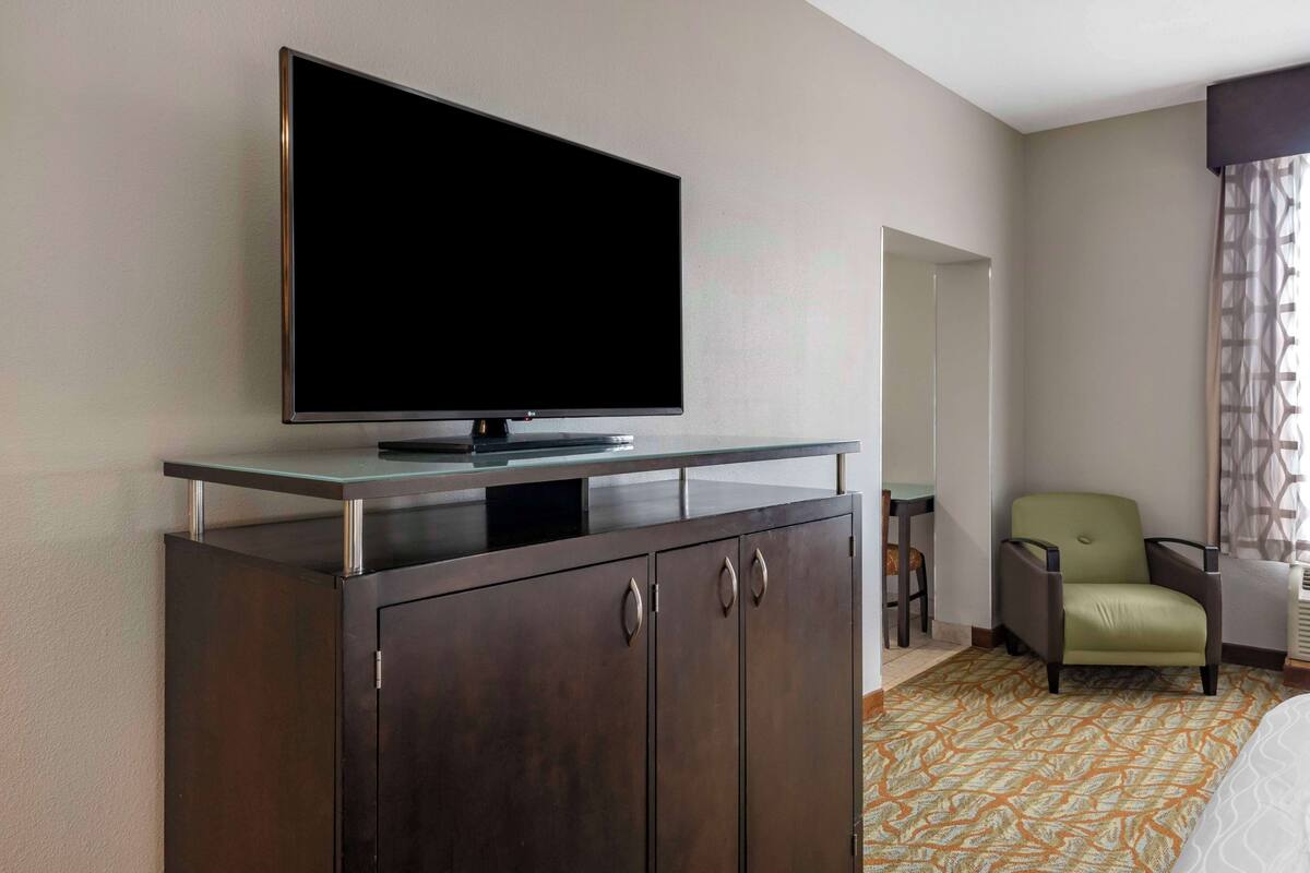 Een hotelkamer met een flatscreen televisie op een kast, een groene stoel en een kamerbreed tapijt met dessin.