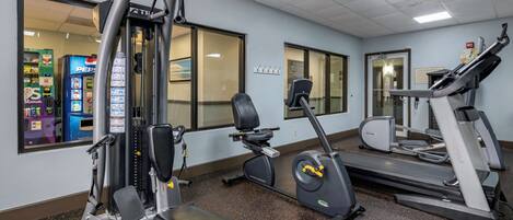 A gym with various exercise equipment including a weight machine, elliptical, and treadmills.