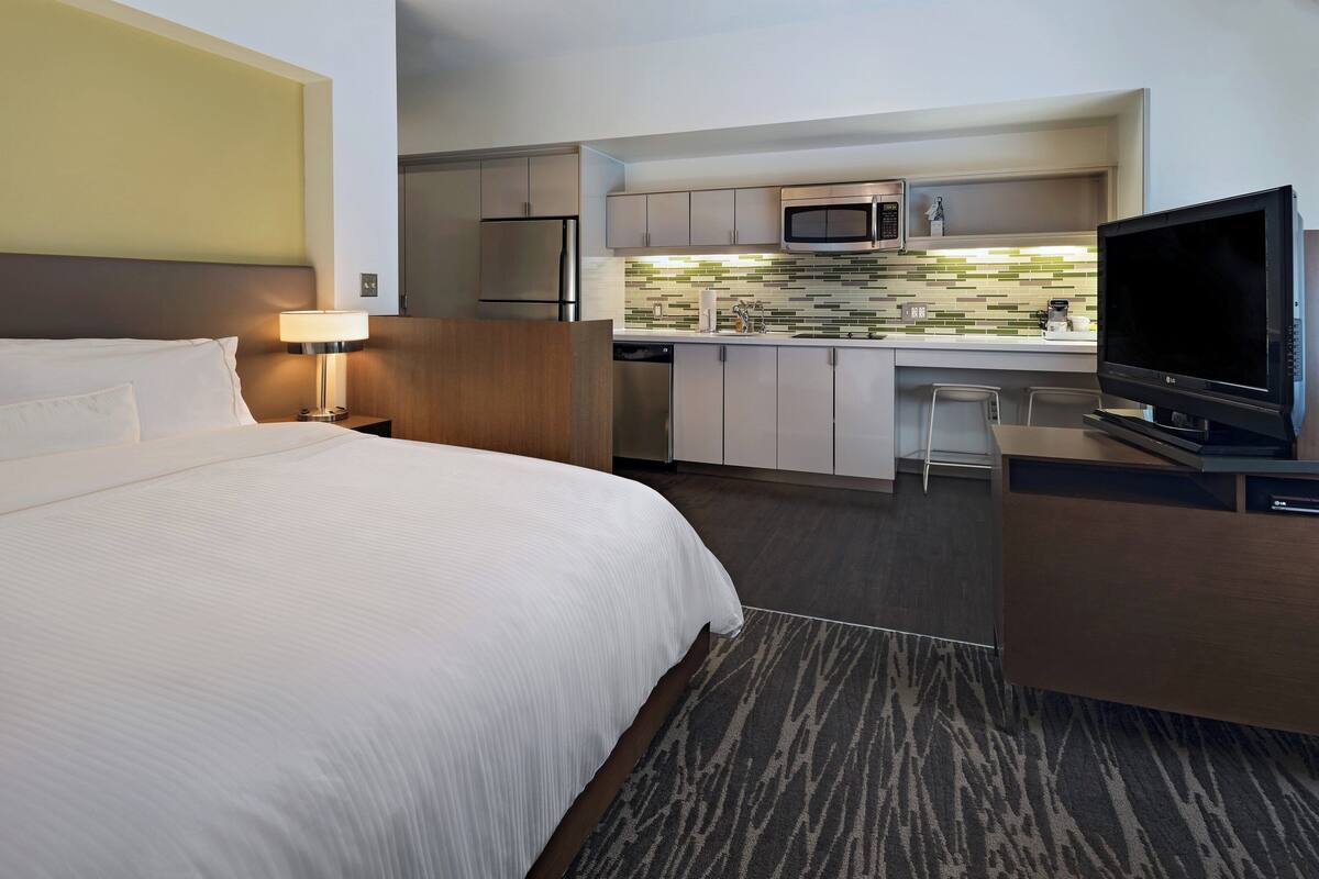 A hotel room with a bed, a desk, a television, a microwave, and a kitchenette.
