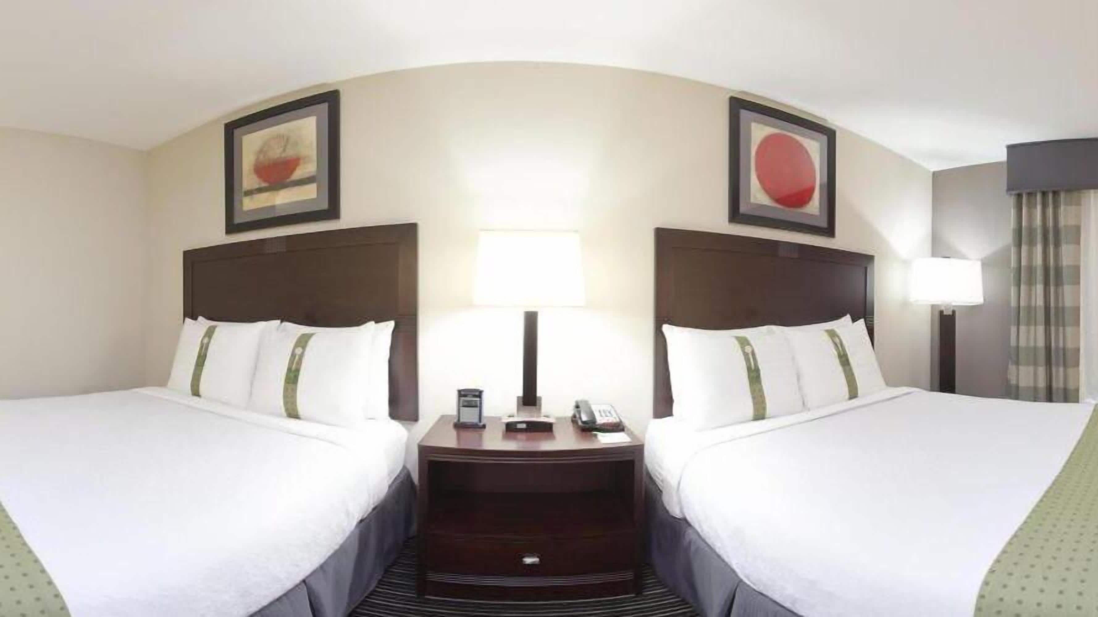 A hotel room with two beds, a nightstand between them, a lamp, and two framed pictures on the walls.