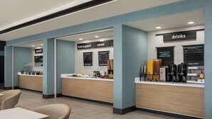 A modern cafe with a counter displaying hot foods, fruit & yogurt, and cereal. There are seating areas with tables and chairs. - Holiday Inn Columbus-Hilliard by IHG (Columbus)