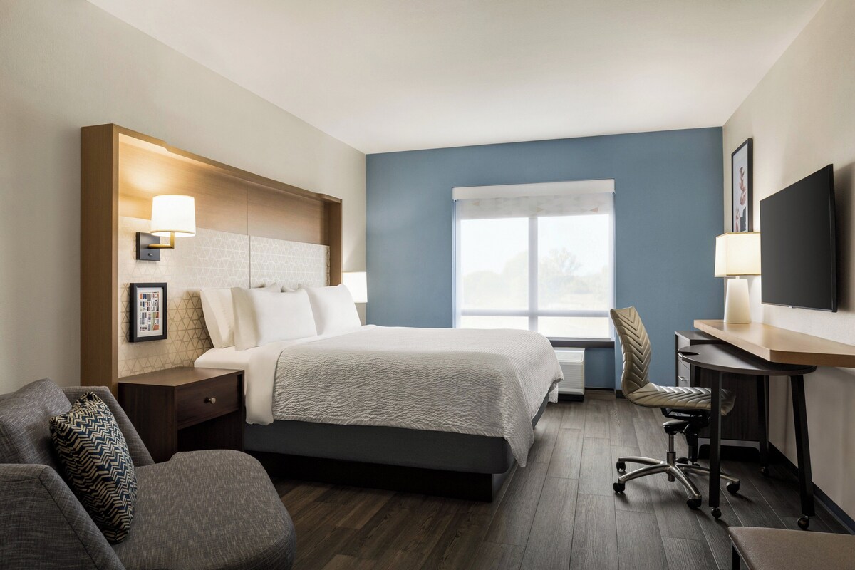 A hotel room with a bed, a desk, a chair, a TV, and a window.