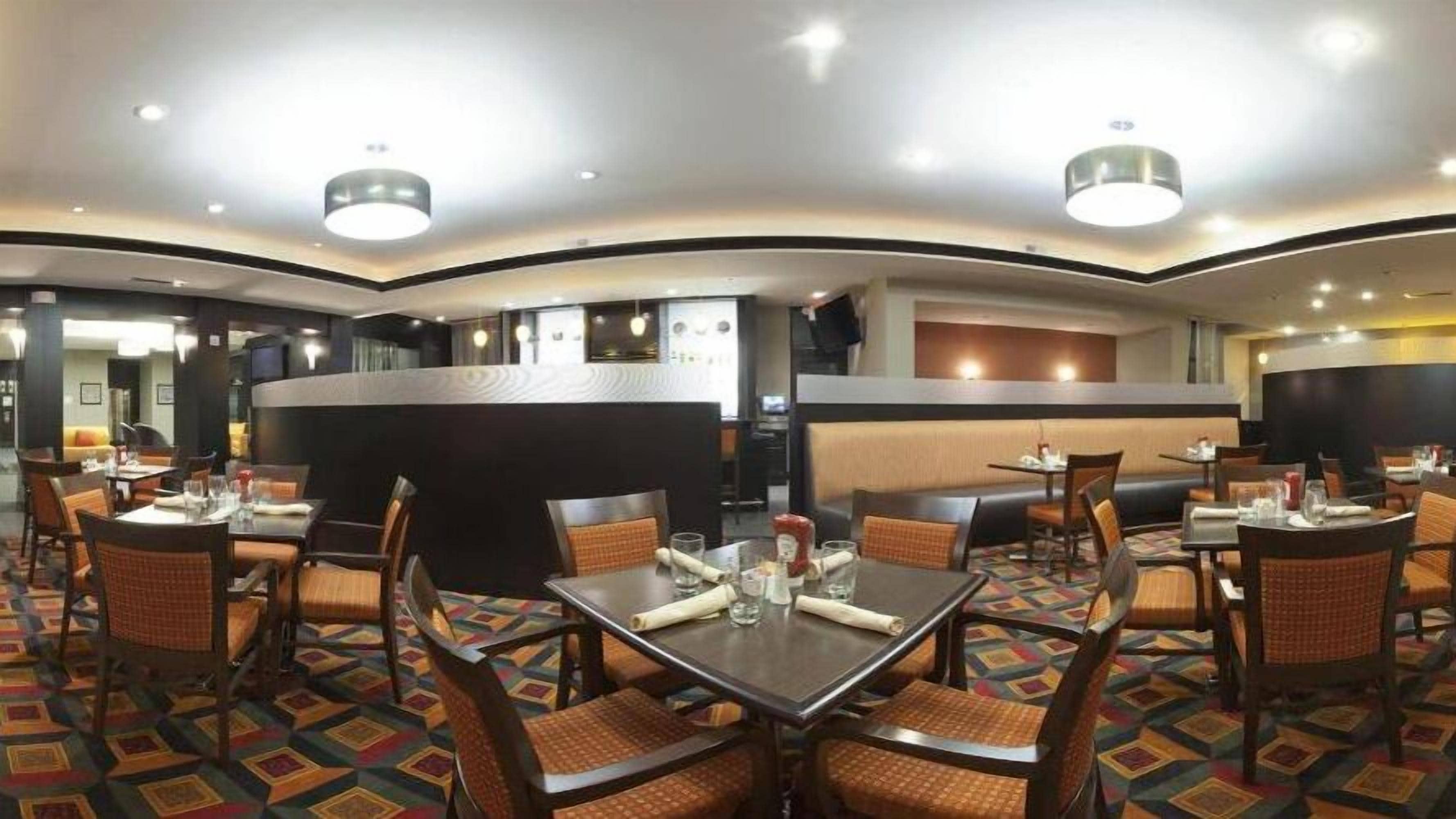 A restaurant with round tables and booths, a central counter, and patterned carpet flooring.