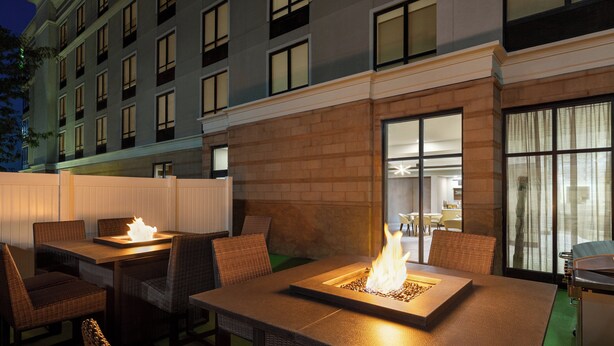 An outdoor patio area with tables and chairs, a fire feature, and a view of a building with multiple windows. - Holiday Inn Columbus-Hilliard by IHG (Columbus)