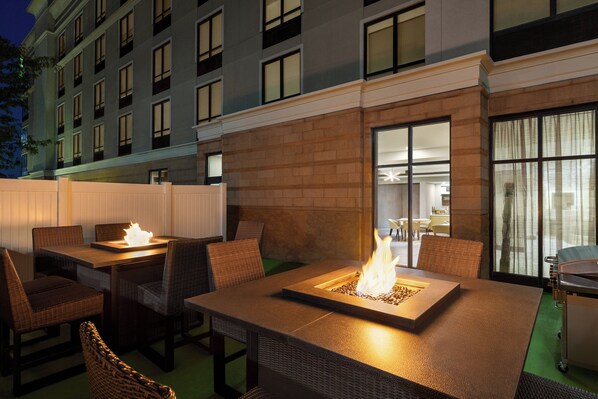 An outdoor patio area with tables and chairs, a fire feature, and a view of a building with multiple windows. - Holiday Inn Columbus-Hilliard by IHG (Columbus)