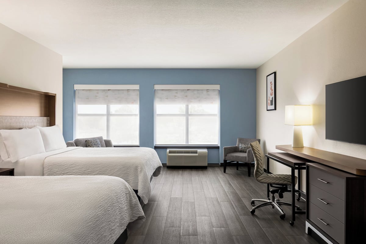 A hotel room with two beds, a desk, a chair, a TV, and a window with a curtain.