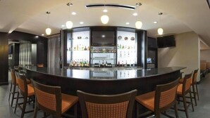 A bar area with a curved counter, multiple seating options, and a variety of bottles and glasses on shelves. - Holiday Inn Columbus-Hilliard by IHG (Columbus)