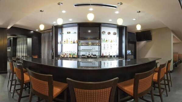 A bar area with a curved counter, multiple seating options, and a variety of bottles and glasses on shelves. - Holiday Inn Columbus-Hilliard by IHG (Columbus)