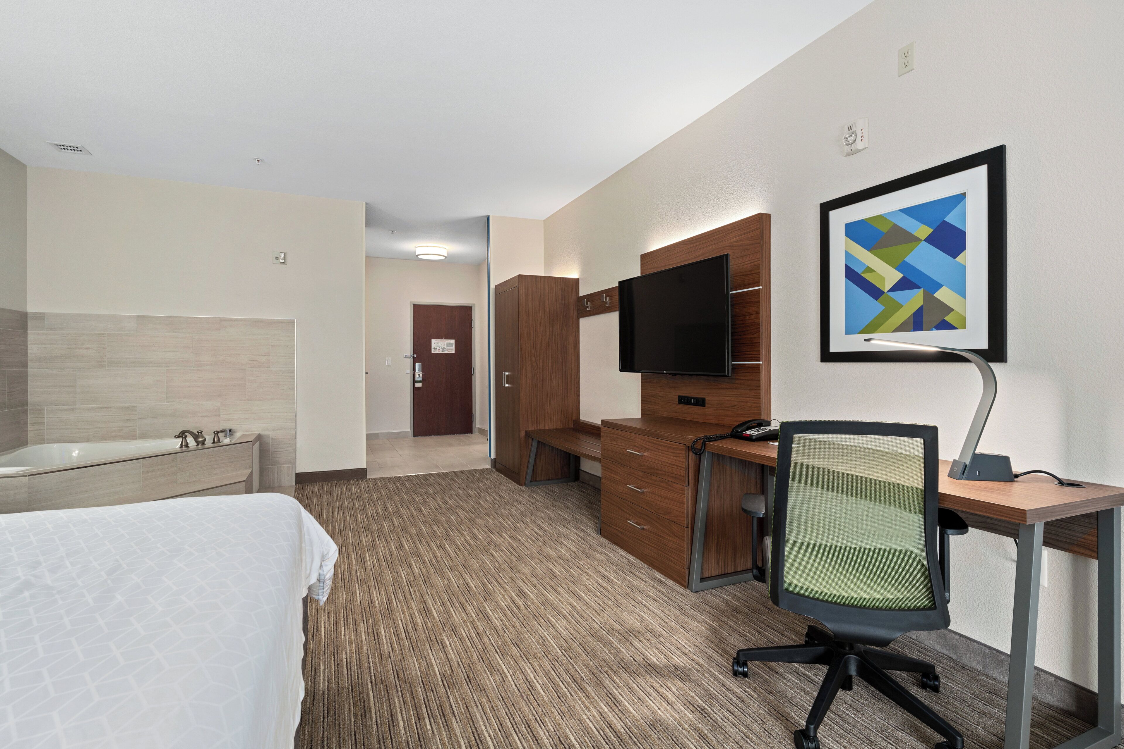 A hotel room with a bed, a desk, a chair, a television, and a bathroom.