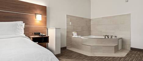 A modern hotel room with a bed, a bedside telephone, a wall-mounted light, a corner bathtub, and a textured floor.